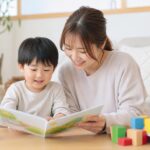 幼児が母親と絵本を見ながら日本語と英語の言葉に楽しくふれる家庭の場面