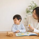 オンライン英会話を少し嫌がる幼児に母親がやさしく寄り添う明るい家庭の場面