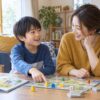家庭でボードゲームを楽しみながら母親と話す小学生のイメージ