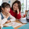母親が見守る中で小学生の子どもが画面の先生に短い言葉を伝えようとするイメージ