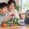 親の見守りのもとで自作のブロックの家を画面越しの友達へ紹介する小学生のイメージ