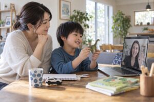 親のそばで好きなおもちゃを画面の先生に見せる子どものイメージ