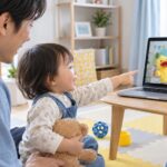 父親のそばで画面の先生の人形を見つめる幼児のイメージ（AI生成）