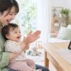 赤ちゃんを膝に抱き、画面の先生と手拍子をする母親のイメージ（AI生成）