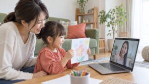 母親の隣でオンラインの先生に絵を見せる子どものイメージ（AI生成）