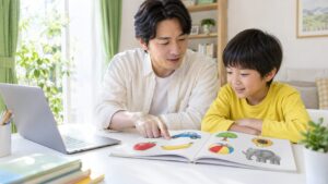 父親と子どもがパソコンのそばで絵本の絵を指さすイメージ（AI生成）