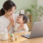 母親の膝で手をたたく幼児とオンライン通話のイメージ（AI生成）