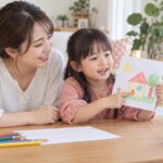 母親と一緒に描いた絵を画面の先生へ見せる幼児のイメージ（AI生成）