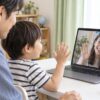 父親と一緒にオンラインの先生へ手を振る幼児のイメージ（AI生成）