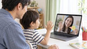父親と一緒にオンラインの先生へ手を振る幼児のイメージ（AI生成）
