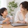 閉じたパソコンのそばで子どもの話を聞く母親のイメージ（AI生成）
