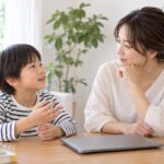 閉じたパソコンのそばで子どもの話を聞く母親のイメージ（AI生成）