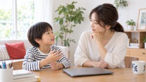 閉じたパソコンのそばで子どもの話を聞く母親のイメージ（AI生成）