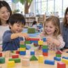 保護者が見守る中、積み木の橋を一緒に作る二人の幼児のイメージ