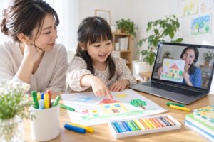 母親の隣でお絵描きをし、画面の先生と絵を見せ合う幼児のイメージ