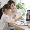 母親が見守る家の机で、海外の友だちに絵を見せる小学生のイメージ
