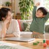 閉じたパソコンから離れて母親の隣で伸びをする子どものイメージ（AI生成）